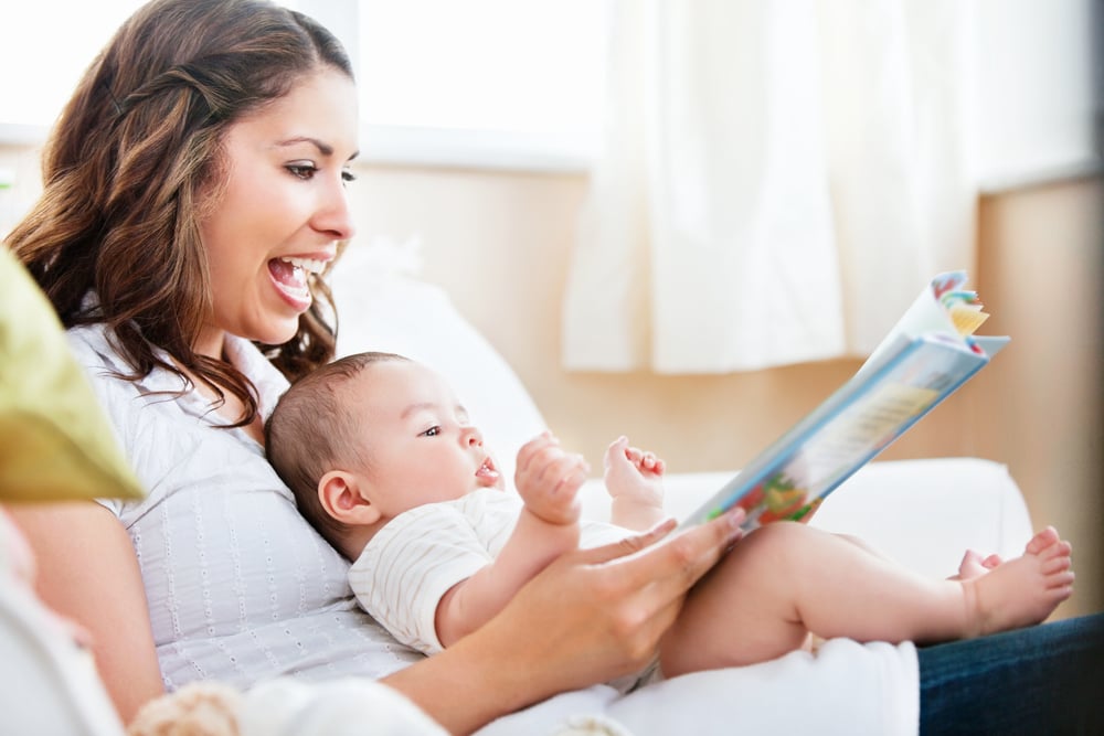 Charming mother showing images in a book to her cute little son at home