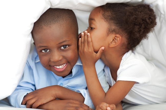 Cute little girl whispering something to her brother under the cover