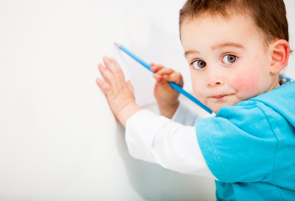 Little boy drawing on a white wall