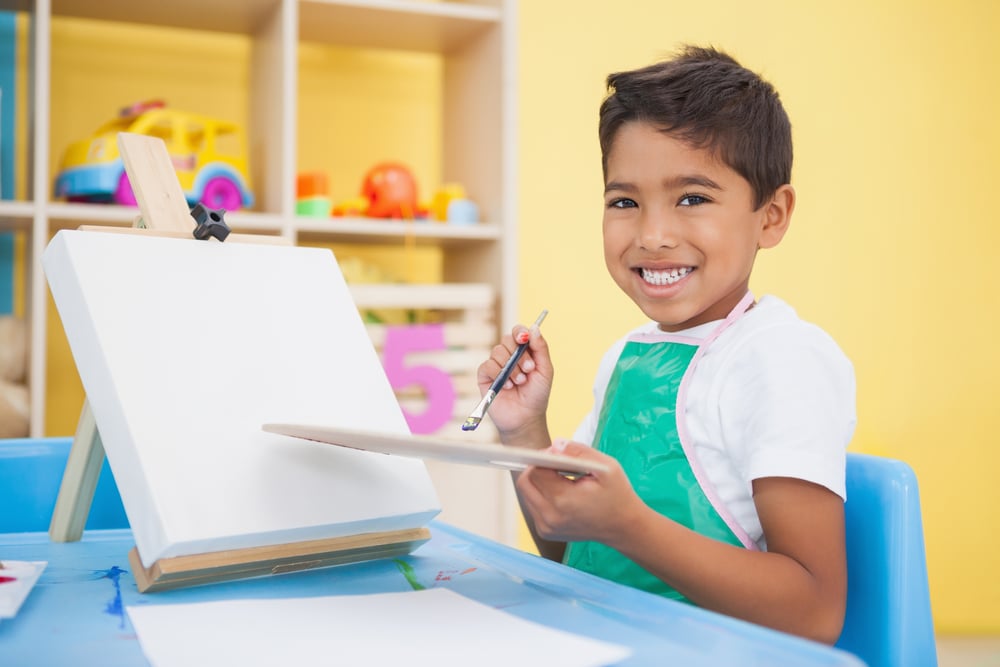 Cute little boy painting at table in classroom at the nursery school