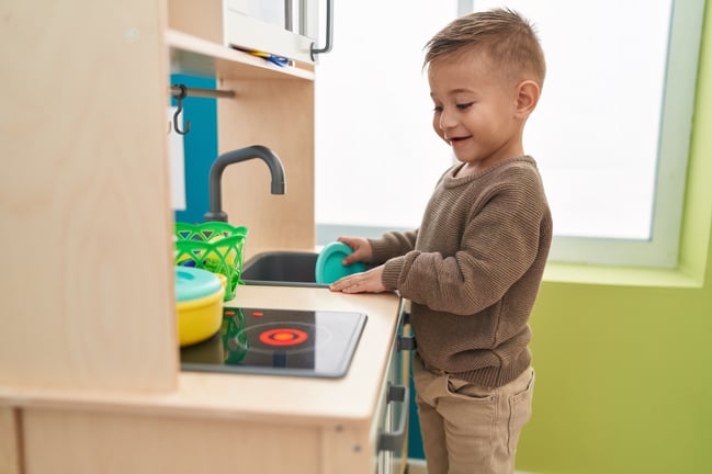 adorable-hispanic-boy-playing-with-play-kitchen-standing-kindergarten