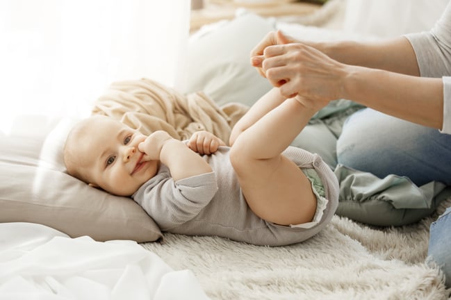 close-up-portrait-little-newborn-son-lying-bed-while-playing-with-mother-kid-smiling-put-his-fingers-mouth-lookin-happy-carefree
