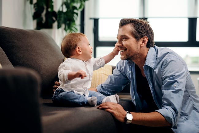 curious-baby-son-touching-father-s-face-while-sitting-sofa-living-room