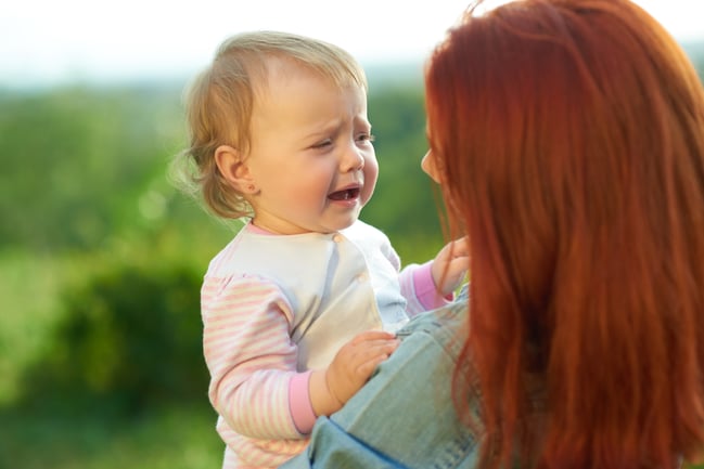 crying-daughter-sitting-mother-s-hands-sunny-day-field-young-mom-trying-calm-down-little-baby-talking-her-woman-having-red-hair-wearing-jeans-shirt
